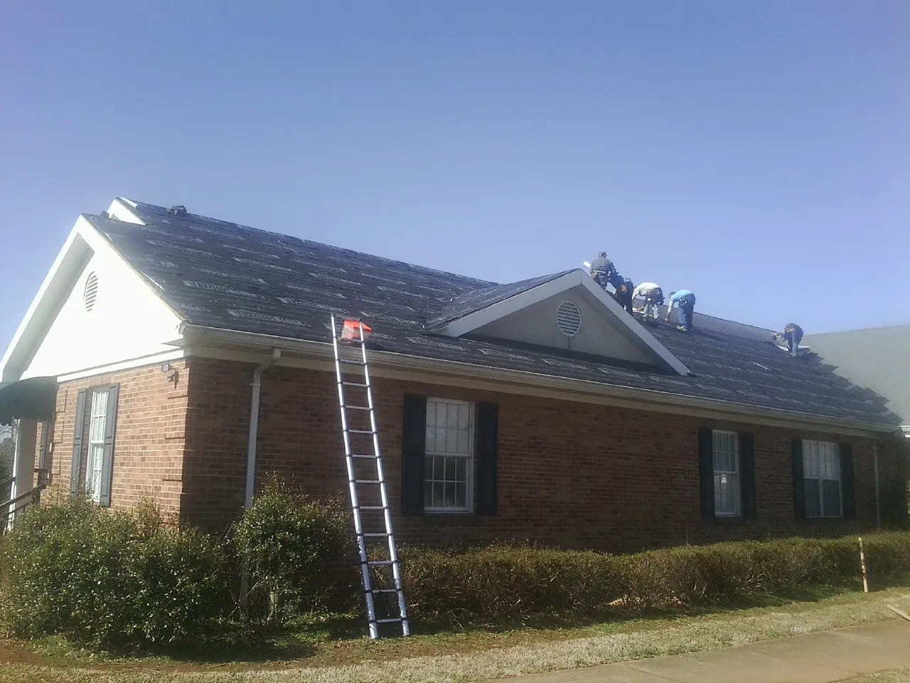 Crew tearing shingles off a brick ranch roof with a ladder set — Metal Roof Repair work by our crew in Pacific Beach
