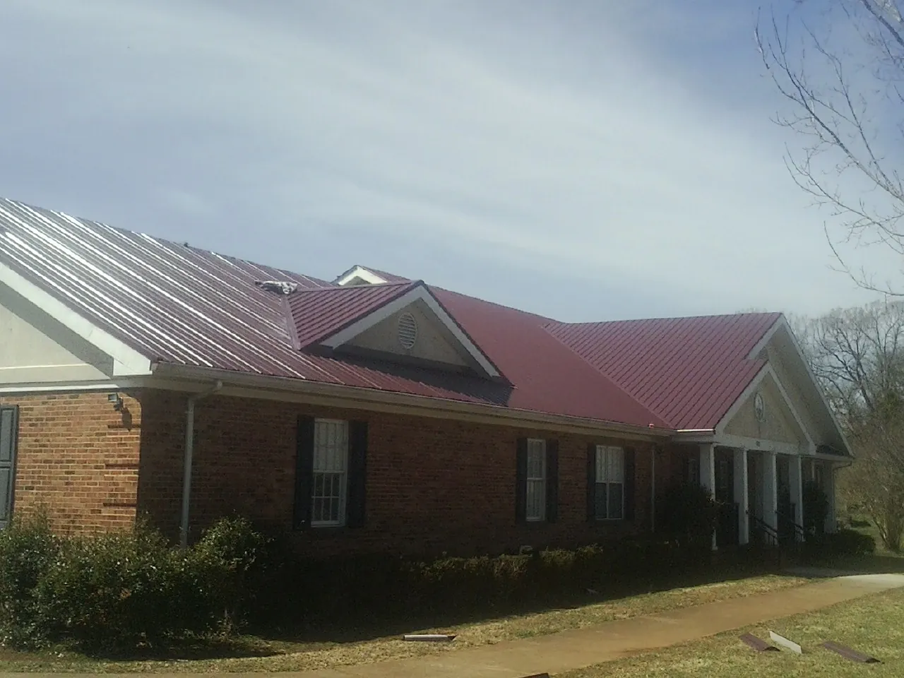 Red metal roof with gabled entries on a long brick building, from a Hail Damage Roof Repair job in Pacific Beach