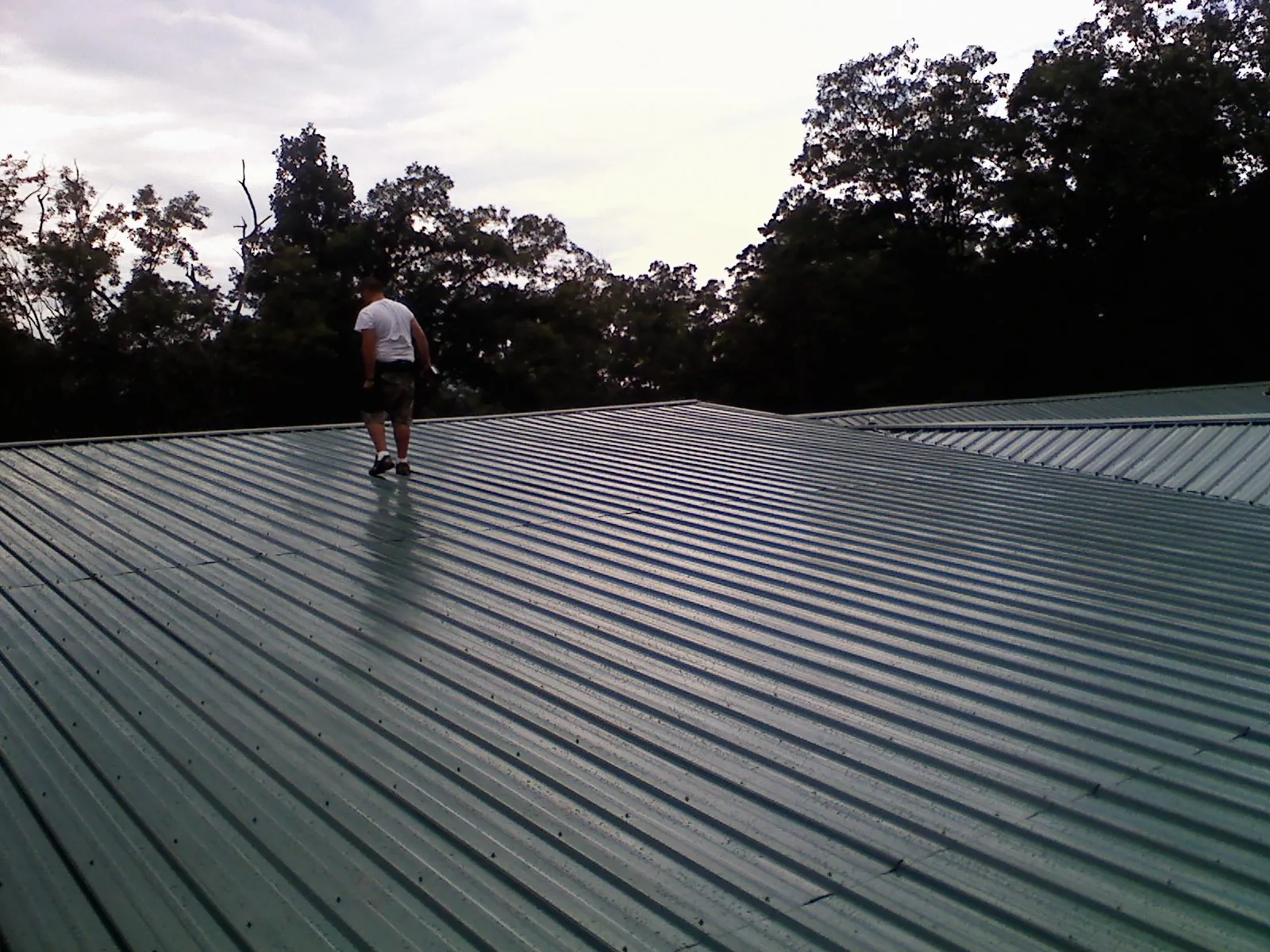 Roofer walking a wide expanse of new green metal roofing in Pacific Beach