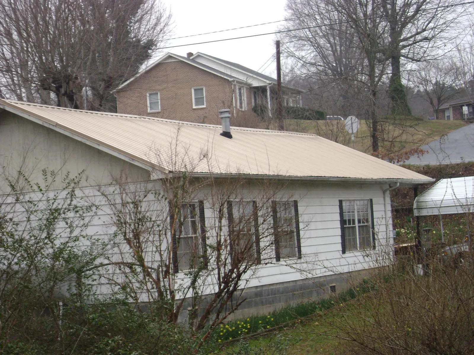 Tan metal roof on a white sided house set into a hillside — Commercial Roofing by Roofing Brothers in Pacific Beach